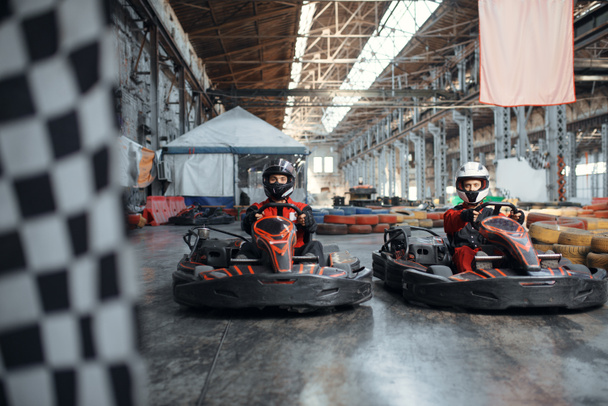 Two kart racers on start line, checkered flag, front view, karting auto sport indoor. Speed race on close go-cart track with tire barrier. Fast vehicle competition, high adrenaline leisure - Foto, afbeelding