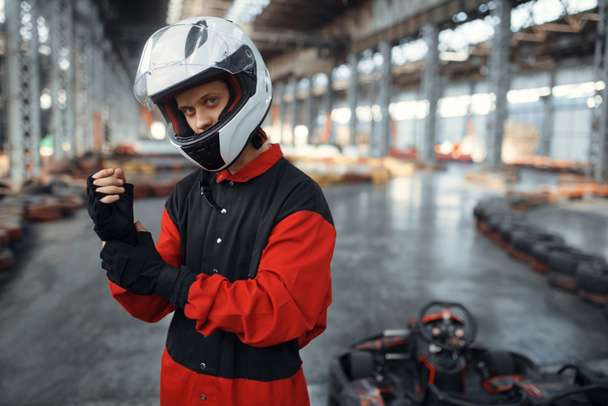 Kart racer in red uniform, helmet and gloves, karting auto sport indoor. Speed race on close go-kart track with tire barrier. Fast vehicle competition, high adrenaline hobby - Photo, Image