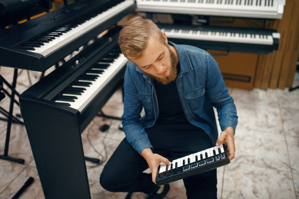 Bearded young musician buying synthesizer in music store. Assortment in musical instrument shop, male musician choosing keyboard - Zdjęcie, obraz
