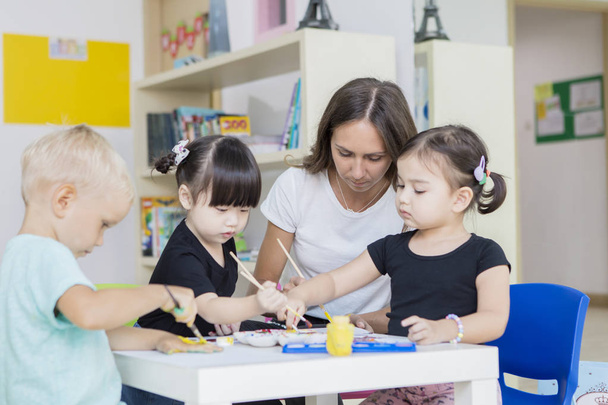 Nursery teacher with her students painting draws - Foto, Imagen