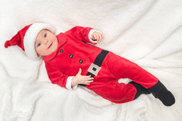 サンタクロースの衣装の小さな赤ちゃんは白い毛布の上に横たわっている - 写真・画像
