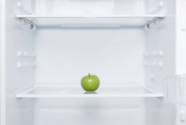 green fresh apple lies on a shelf in an open white refrigerator - Foto, immagini