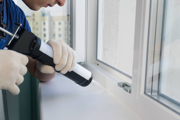 a man works with silicone sealant to insulate windows from dust and dirt in the house - Photo, Image