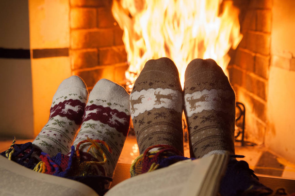 Homem e mulher em meias de malha quente com xícaras de soco quente na frente da lareira
 - Foto, Imagem