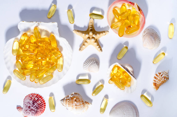 Omega-3-Kapseln und Muscheln mit langen Schatten. Foto von oben von Nahrungsergänzungsmitteln mit Öl nordischer Fische. Vitamine und Tabletten gegen Weiß. - Foto, Bild