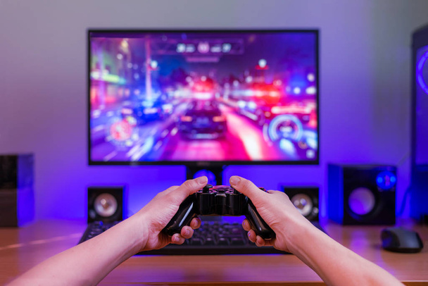 Joypad in hands. Computer gaming concept. Computer display with game in background. RGB light behind the desk. - Photo, image