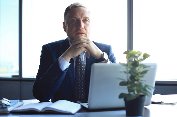 Focused mature businessman deep in thought while sitting at a table in modern office. - 写真・画像