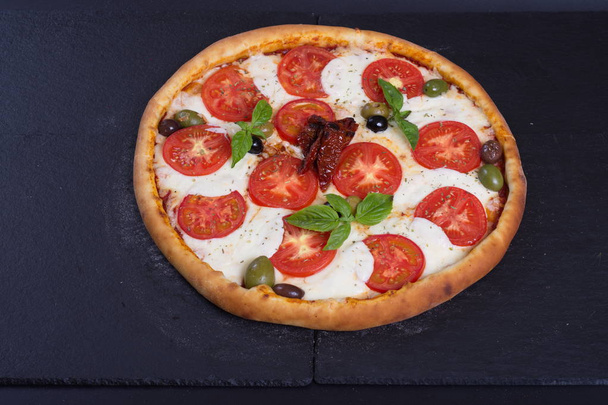pizza with tomatoes cheese and meat lies on a black stone - Photo, image