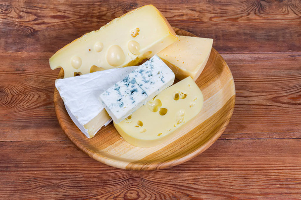Peças de queijo diferente em prato de madeira em mesa rústica
 - Foto, Imagem