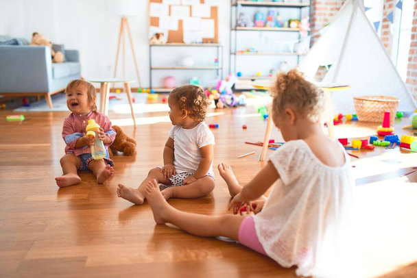 Niños adorables sentados en el suelo jugando alrededor de muchos juguetes en el jardín de infantes
 - Foto, imagen