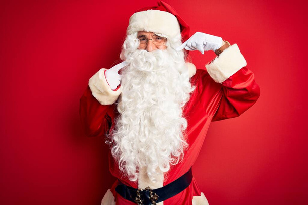 Keski-ikä komea mies yllään Santa puku seisoo yli eristetty punainen tausta hymyillen iloinen osoittaa ja sormilla hampaat ja suu. Hammasterveyden käsite
. - Valokuva, kuva