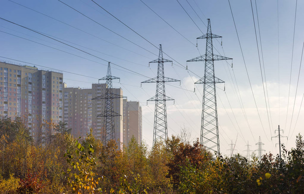 Líneas eléctricas aéreas sobre árboles de otoño contra edificios de varios pisos
 - Foto, Imagen