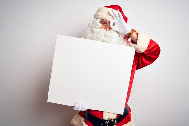 Hombre de mediana edad con disfraz de Papá Noel sosteniendo pancarta sobre fondo blanco aislado con la cara feliz sonriendo haciendo signo bien con la mano en el ojo mirando a través de los dedos
 - Foto, Imagen