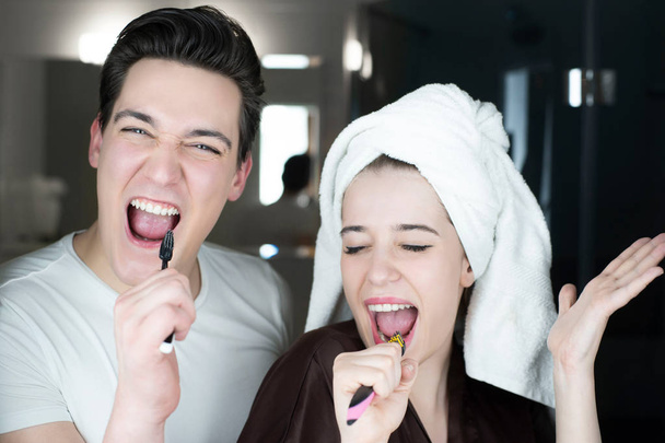 young couple handsome smiling man and beautiful woman in turban with toothbrushes in their hands singing in bathroom in the morning looking happy everyday routine - Fotoğraf, Görsel