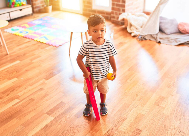Beautiful toddler boy playing tennis with red racket and ball at kindergarten - Photo, image