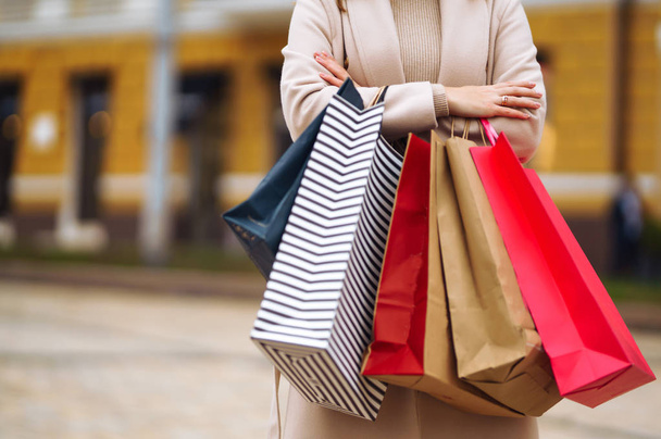 Shopping bags in the hands. Hand of young woman with multi-coloured bags with purchases. Beautiful girl holding shopping bags on the city street. Consumerism, shopping, sales, lifestyle concept.  - 写真・画像