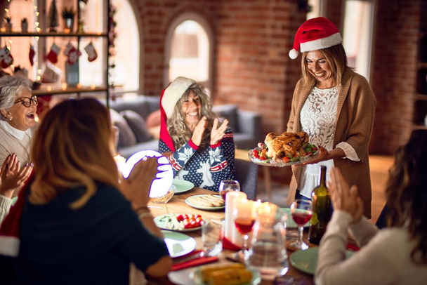 schöne Gruppe von Frauen, die glücklich und zuversichtlich lächeln. zeigt gebratenen Truthahn, der zu Hause Weihnachten feiert - Foto, Bild