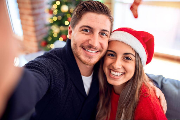 Mutlu ve kendinden emin gülümseyen genç bir çift. Evdeki Noel ağacının etrafında kamerayla selfie çekmek. - Fotoğraf, Görsel