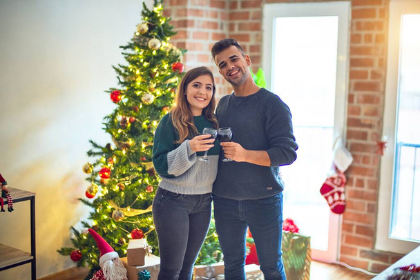 Young beautiful couple smiling happy and confident. Toasting with cup of wine celebrating christmas at home - Photo, Image