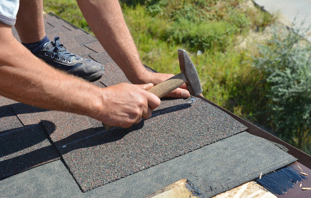Roofing Construction. Roofer with hammer and nails laying asphalt shingles tiles on house roof.  - Φωτογραφία, εικόνα