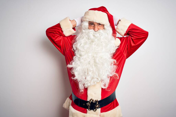 gutaussehender Mann mittleren Alters im Weihnachtsmannkostüm, der vor isoliertem weißem Hintergrund steht und sich entspannt und dehnt, Arme und Hände hinter Kopf und Hals lächelnd glücklich - Foto, Bild