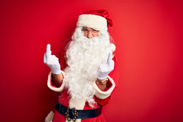 Middle age handsome man wearing Santa costume standing over isolated red background Showing middle finger doing fuck you bad expression, provocation and rude attitude. Screaming excited - Φωτογραφία, εικόνα