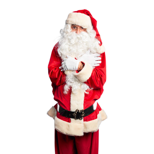 Middle age handsome man wearing Santa Claus costume and beard standing shaking and freezing for winter cold with sad and shock expression on face - Fotó, kép