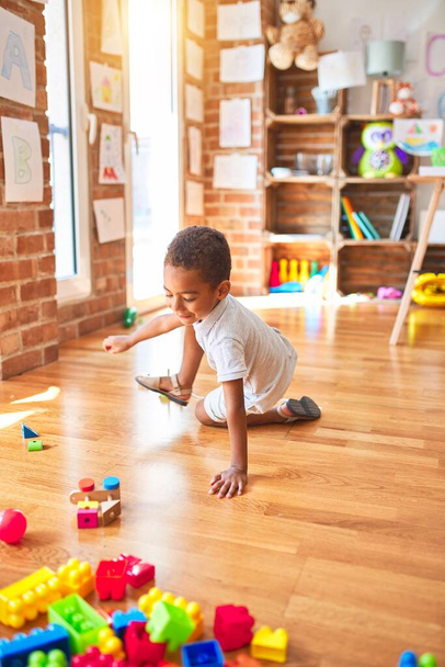 Hermoso niño afroamericano jugando con bloques de madera tren juguete alrededor de un montón de juguetes en el jardín de infantes
 - Foto, Imagen