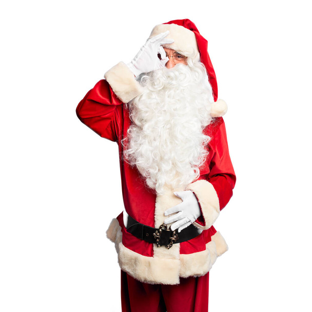 gutaussehender Mann mittleren Alters im Weihnachtsmann-Kostüm und Bart stehend und mit lächelnder Hand eine gute Geste machend, mit glücklichem Gesicht durch die Finger blickend. - Foto, Bild