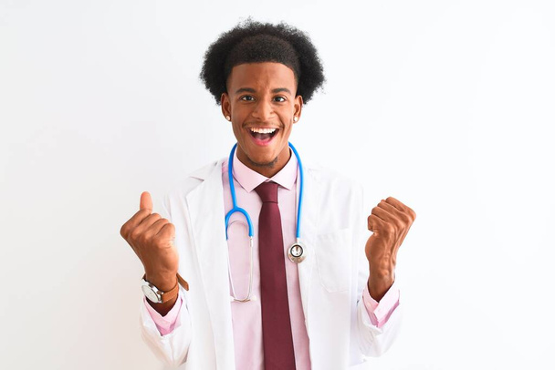 Jonge Afro-Amerikaanse arts draagt sthetoscoop over geïsoleerde witte achtergrond vieren verrast en verbaasd voor succes met opgeheven armen en open ogen. Winnaars concept. - Foto, afbeelding
