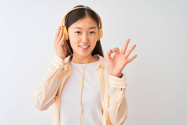 Nuori kiinalainen nainen kuuntelee musiikkia kuulokkeilla yli eristetty valkoinen tausta tekee ok merkki sormilla, erinomainen symboli
 - Valokuva, kuva