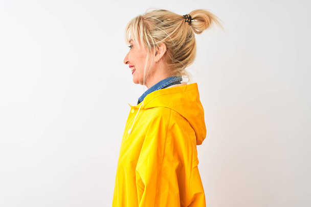 Mujer de mediana edad con abrigo de lluvia amarillo de pie sobre fondo blanco aislado mirando a un lado, pose de perfil relajante con cara natural con sonrisa confiada
. - Foto, imagen