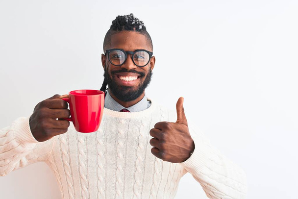 Afro-Amerikaanse man met vlechten drinken kopje koffie over geïsoleerde witte achtergrond blij met grote glimlach doet ok teken, duim omhoog met vingers, uitstekend teken - Foto, afbeelding