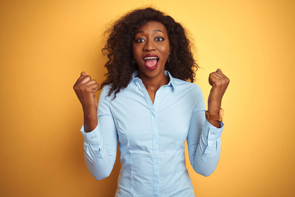 African american businesswoman wearing elegant shirt over isolated yellow background celebrating surprised and amazed for success with arms raised and open eyes. Winner concept. - 写真・画像