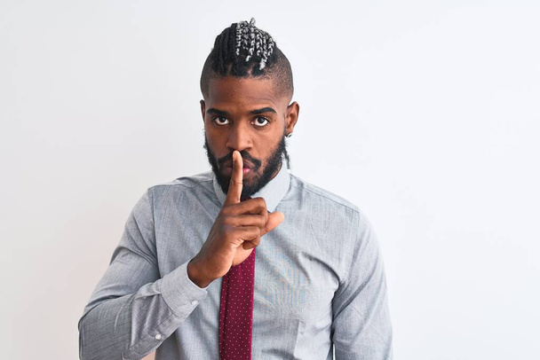 Afrikai-amerikai üzletember fonott nyakkendővel, elszigetelt fehér háttér fölött állva, azt kérve, hogy maradjon csendben ujjal a száján. Csend és titkos koncepció. - Fotó, kép