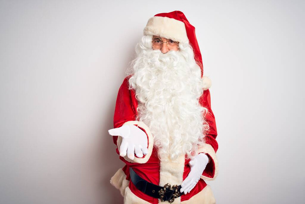 Keski-ikä komea mies yllään Santa puku seisoo yli eristetty valkoinen tausta hymyillen iloinen tarjoaa kämmen antaa apua ja hyväksyntää
. - Valokuva, kuva