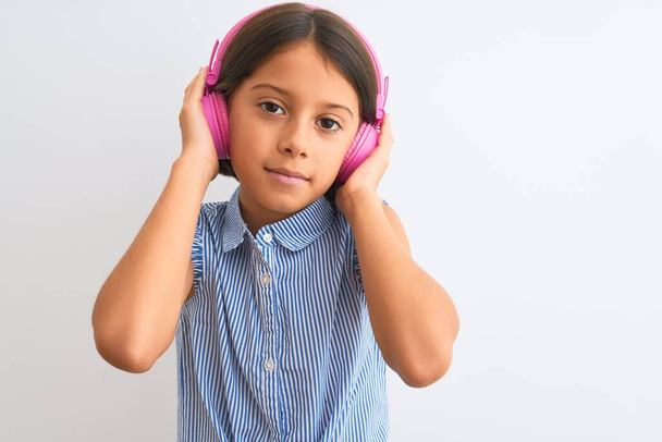 Hermosa niña escuchando música usando auriculares sobre un fondo blanco aislado con una expresión segura en la cara inteligente pensando en serio
 - Foto, imagen