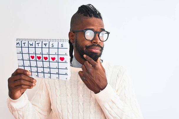 Uomo afroamericano con trecce in possesso di calendario periodo su sfondo bianco isolato volto serio pensando alla domanda, idea molto confusa
 - Foto, immagini