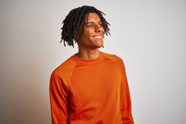 Afro american man with dreadlocks wearing orange sweater over isolated white background looking away to side with smile on face, natural expression. Laughing confident. - Fotografie, Obrázek