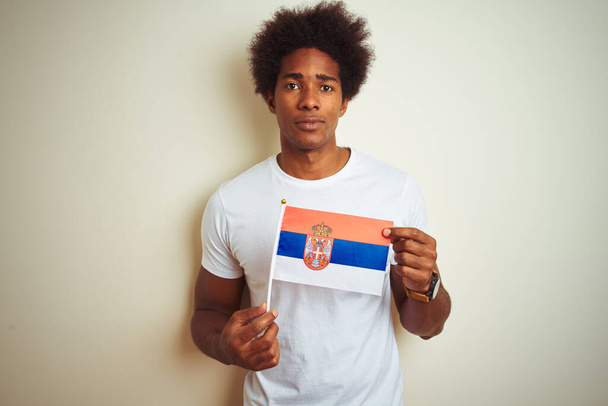 junger afroamerikanischer Mann mit serbischer Flagge auf isoliertem weißem Hintergrund mit selbstbewusstem Gesichtsausdruck und ernstem Denken - Foto, Bild