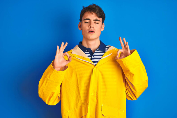 Teenager fisherman boy wearing yellow raincoat over isolated background relax and smiling with eyes closed doing meditation gesture with fingers. Yoga concept. - Photo, Image