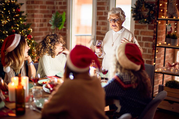 Группа женщин улыбается счастливая и уверенная. На одном из них за чашкой вина произносят речь, празднуя Рождество дома
 - Фото, изображение
