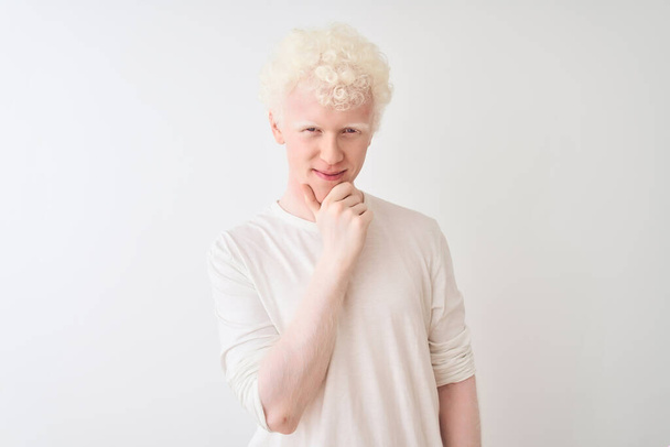 Nuori albiino vaalea mies päällään rento t-paita seisoo yli eristetty valkoinen tausta näyttää luottavainen kameran hymyillen ristissä kädet ja käsi nostetaan leuka. Positiivista.
. - Valokuva, kuva