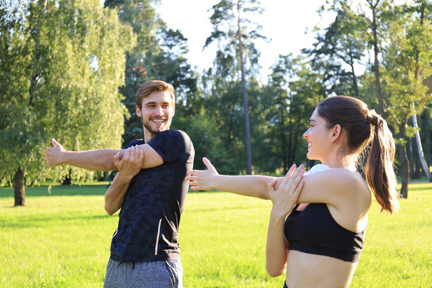 Young couple stretching muscles outdoors in park at sunny day. - Foto, Imagen