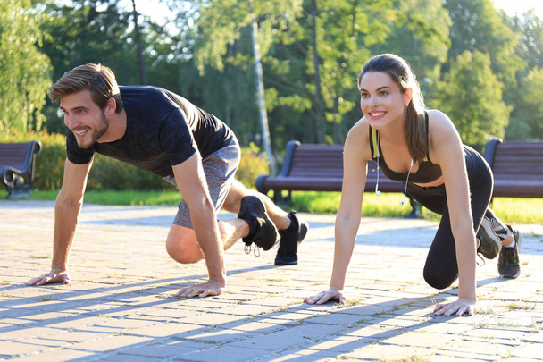 Young couple doing exercise together while working out outdoors in park. - Photo, image
