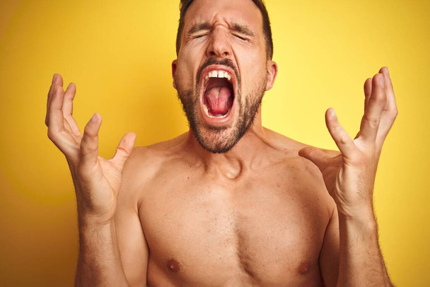 Sexy mladý muž bez trička ukazuje nahý fitness hrudník přes žluté izolované pozadí slaví šílený a šílený pro úspěch s rukama zvednutýma a zavřenýma očima křičí vzrušeně. Koncept vítěze - Fotografie, Obrázek