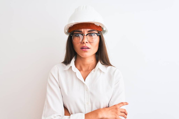 Молодая красивая архитектор женщина в шлеме и очках на изолированном белом фоне скептически и нервно, неодобрительное выражение лица со скрещенными руками. Отрицательное лицо
. - Фото, изображение