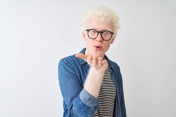 Nuori albiino vaalea mies yllään denim paita ja lasit yli eristetty valkoinen tausta katsot kameraa puhaltaa suudelma käsin ilmassa on ihana ja seksikäs. Rakkauden ilme
. - Valokuva, kuva