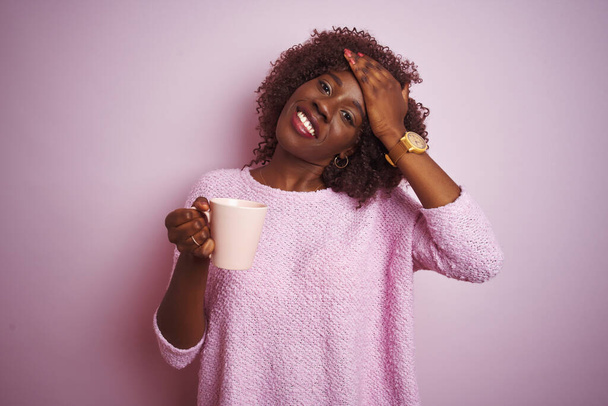 Молодая африканская женщина с чашкой кофе, стоящая на изолированном розовом фоне, напряженная рукой на голове, шокированная стыдом и удивлением, сердитая и расстроенная. Страх и разочарование по ошибке
. - Фото, изображение