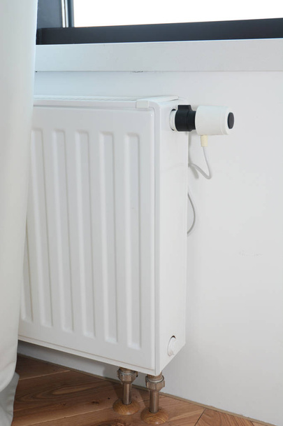 Cacher les tuyaux de radiateur. Chauffage par radiateur blanc avec thermostat pour économiser l'énergie dans la pièce de la maison et les caloducs cachés sous le sol
 - Photo, image
